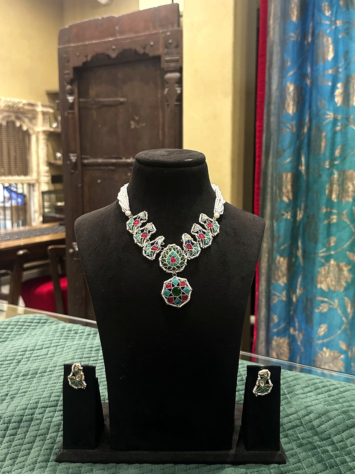 Jadtar pearl necklace set with green and ruby pendant and matching earrings on black velvet bust – Studio Gulabi 926HAI116